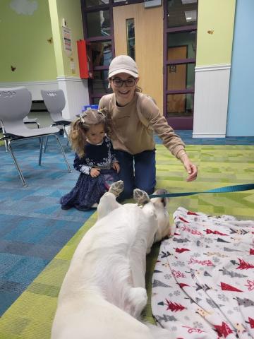 Teddy the yellow Labrador Retriever is lying on his back while a mother and daughter are smiling at him. 